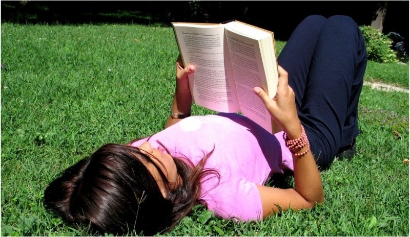 Žena ležící na trávě a drží knihu 