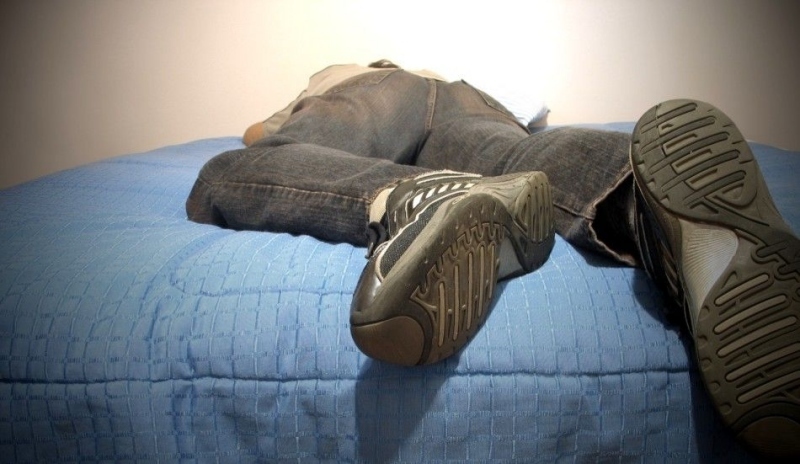 Muž s botami ležící na posteli 