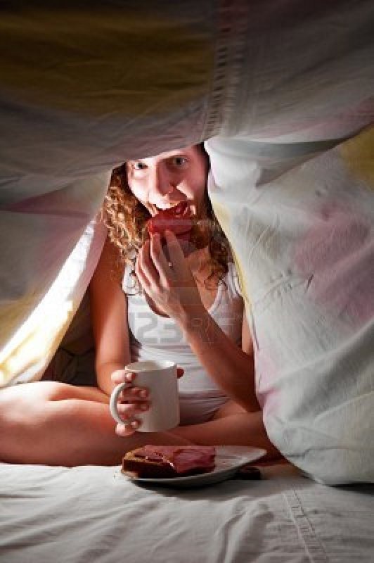 Žena s jídlem a hrnkem schovaná pod peřinou 