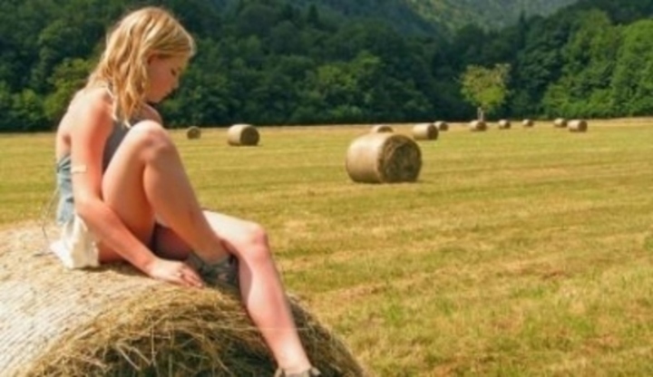 Dívka sedící na otepi slámy uprostřed pole s lesem v pozadí