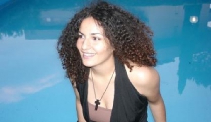 Žena s kudrnatými vlasy a křížkem na krku u bazénu 