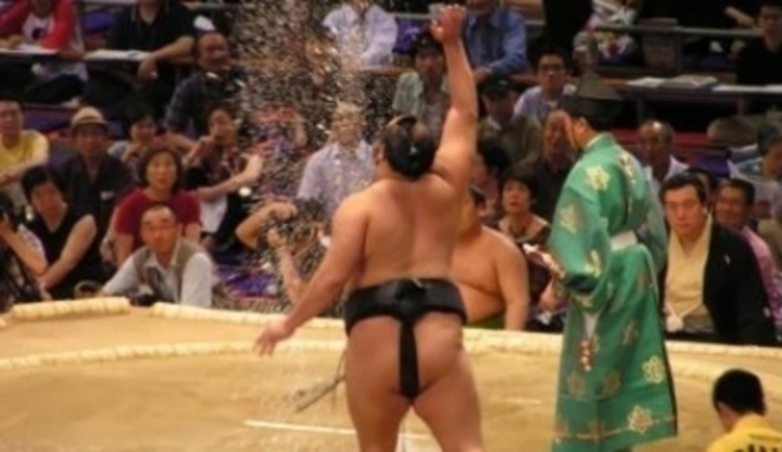 Japonský muž v sumo oblečení se zvednutou rukou, vedle stojící muž v kimonu