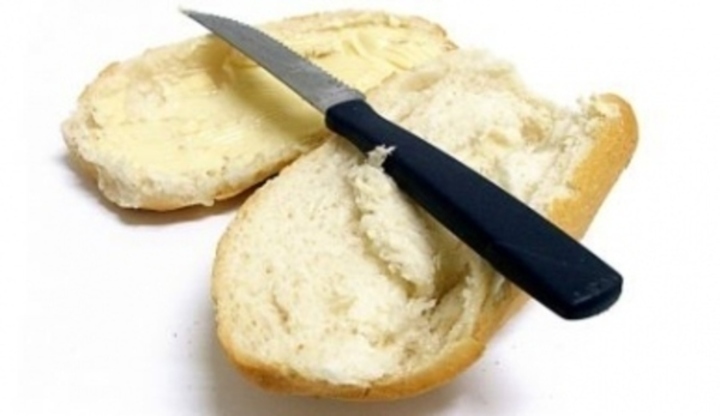 Nůž položený na rozkrojené housce s máslem