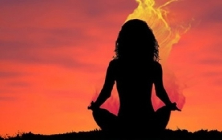 Zády sedící postava meditující ženy při západu slunce