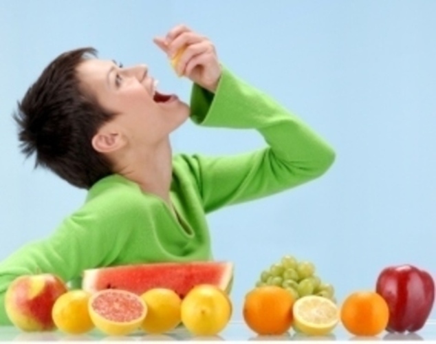 Žena s citronem v ruce sedící u stolu plného ovoce 