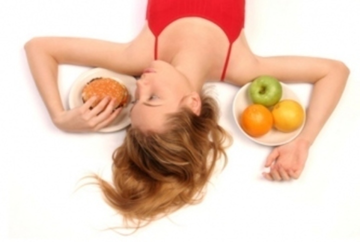 Žena ležící mezi talíři s hamburgrem a ovocem 