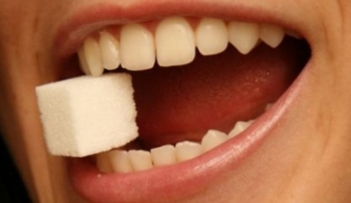 Otevřená ústa s bílými zuby držícími kostku cukru