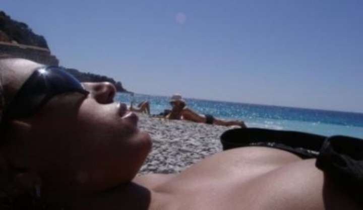 Žena se slunečními brýlemi leží na pláži