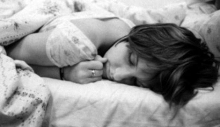 Žena ležící v posteli přikrytá peřinou