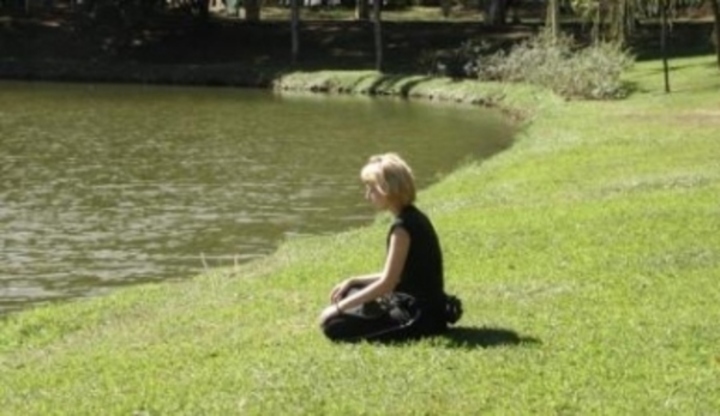 Žena sedící na trávě u vody