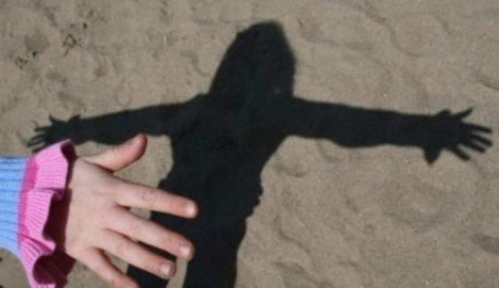 Stín osoby v písku s roztaženýma rukama