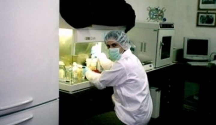 Muž v bílém plášti a roušce sedící u laboratorního stolu