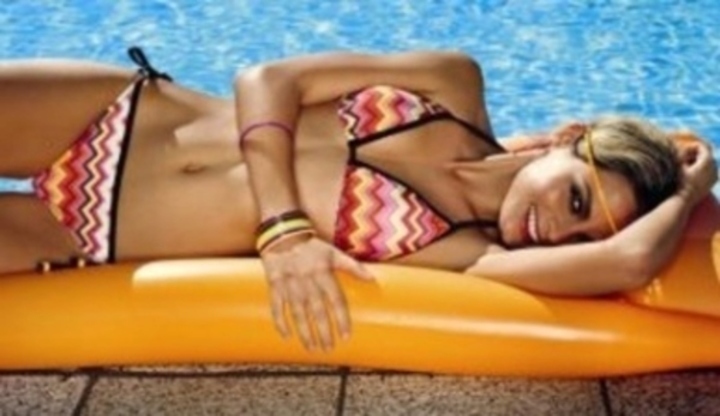 Žena v plavkách ležící na lehátku u bazénu 