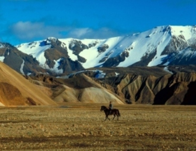 Muž na koni projíždí krajinou kolem hor 