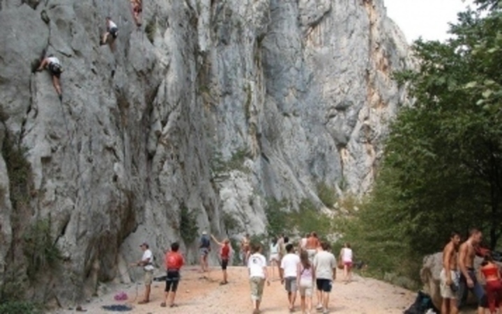 Lidé procházející kolem skal, na které lezou horolezci