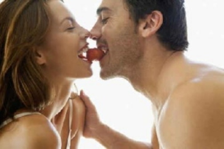 Žena s mužem držící v ústech jahodu 