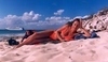 Žena ležící na pláži s hlavou opřenou o ruku 