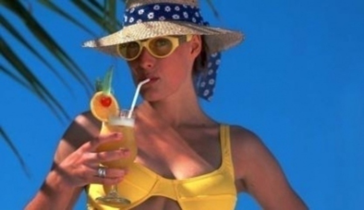 Žena v klobouku a žlutých plavkách  držící sklenici nápoje