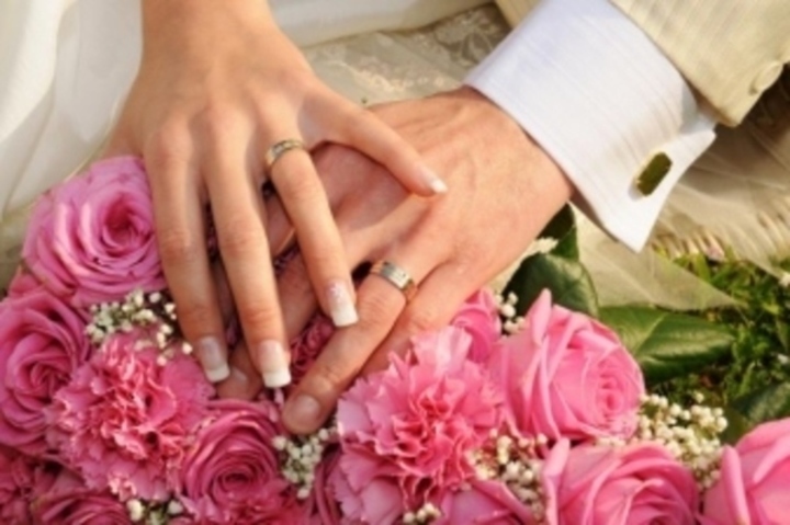 Ruce se snubními prsteny položené na kytici růží 