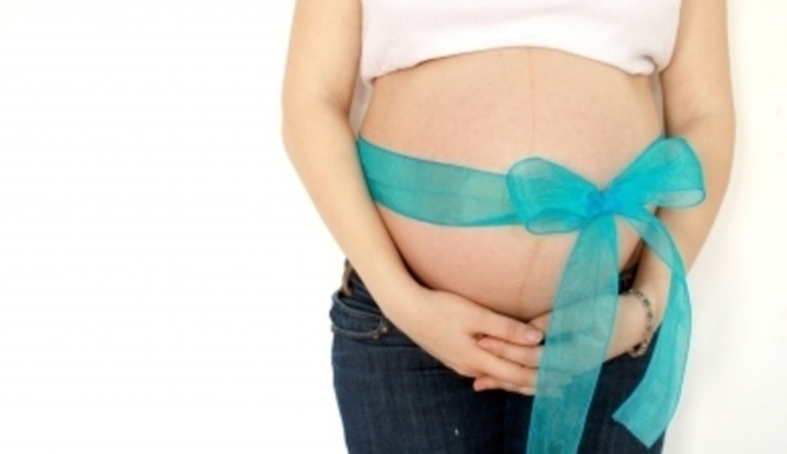 Těhotná žena s modrou mašlí zavázanou přes břicho 