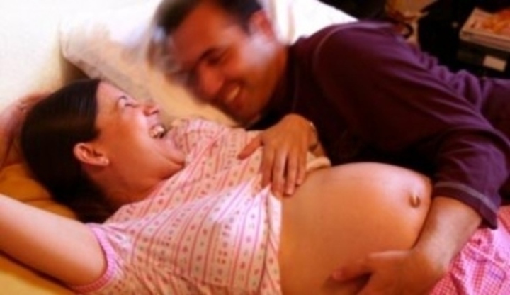 Muž ležící vedle těhotné ženy a objímající její břicho