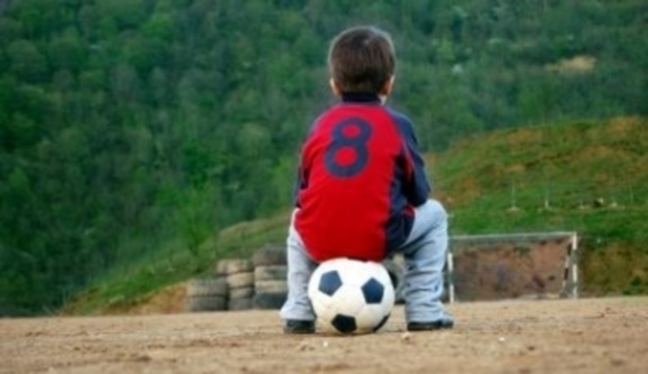 Chlapec sedící zády na fotbalovém míči 