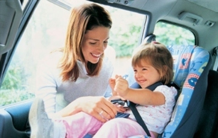 Žena zapínající dítě do autosedačky 