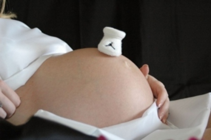 Botička pro dítě položená na bříšku těhotné ženy 
