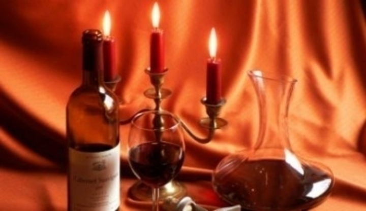Láhev se sklenicí vína, karafou a otvírákem při světle svíček 