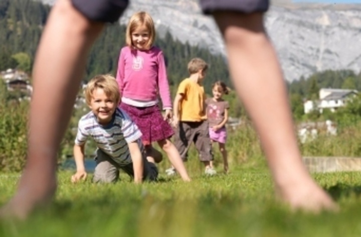 Rozkročené nohy, v pozadí děti hrající si na trávě 