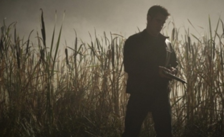Muž s pistolí stojící ve vysoké trávě 