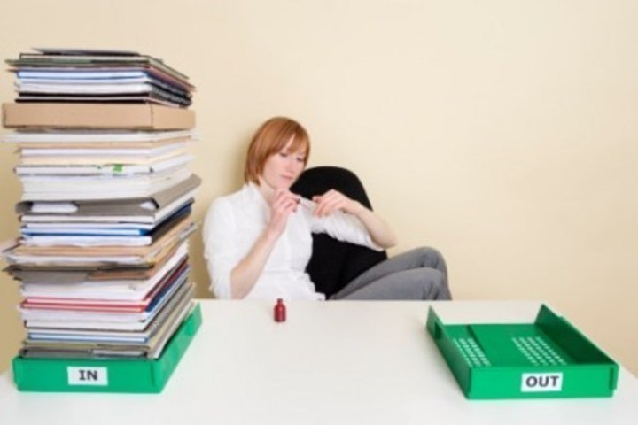 Žena lakující si nehty u stolu plném papírů 