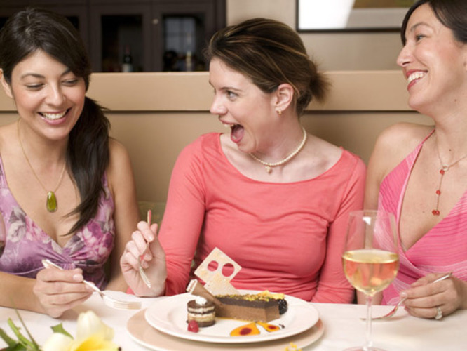Smějící se ženy sedící nad talířem zákusků s vidličkami v ruce 