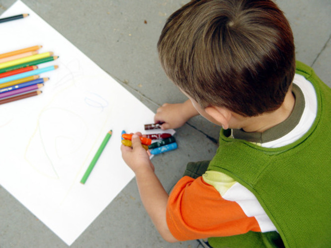 Chlapec kreslící pastelkami na papír 