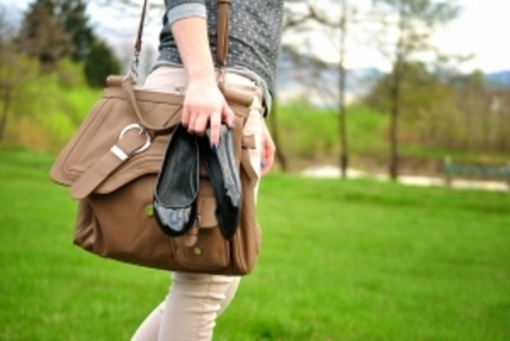 Žena s kabelkou přes rameno držící v ruce boty 