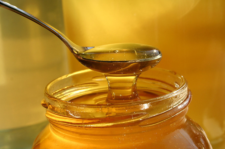 Lžička s medem nad sklenicí medu